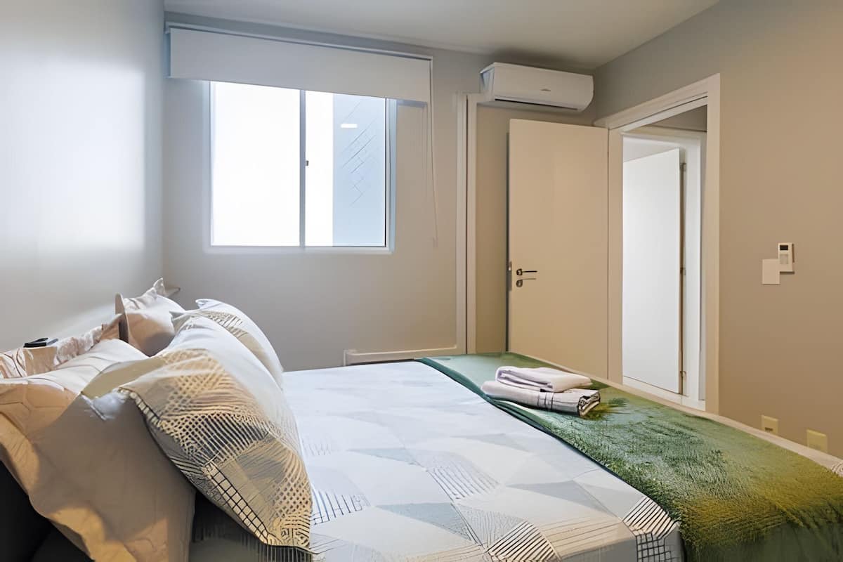 A bedroom with a bed, a window, an air conditioning unit, and a door.