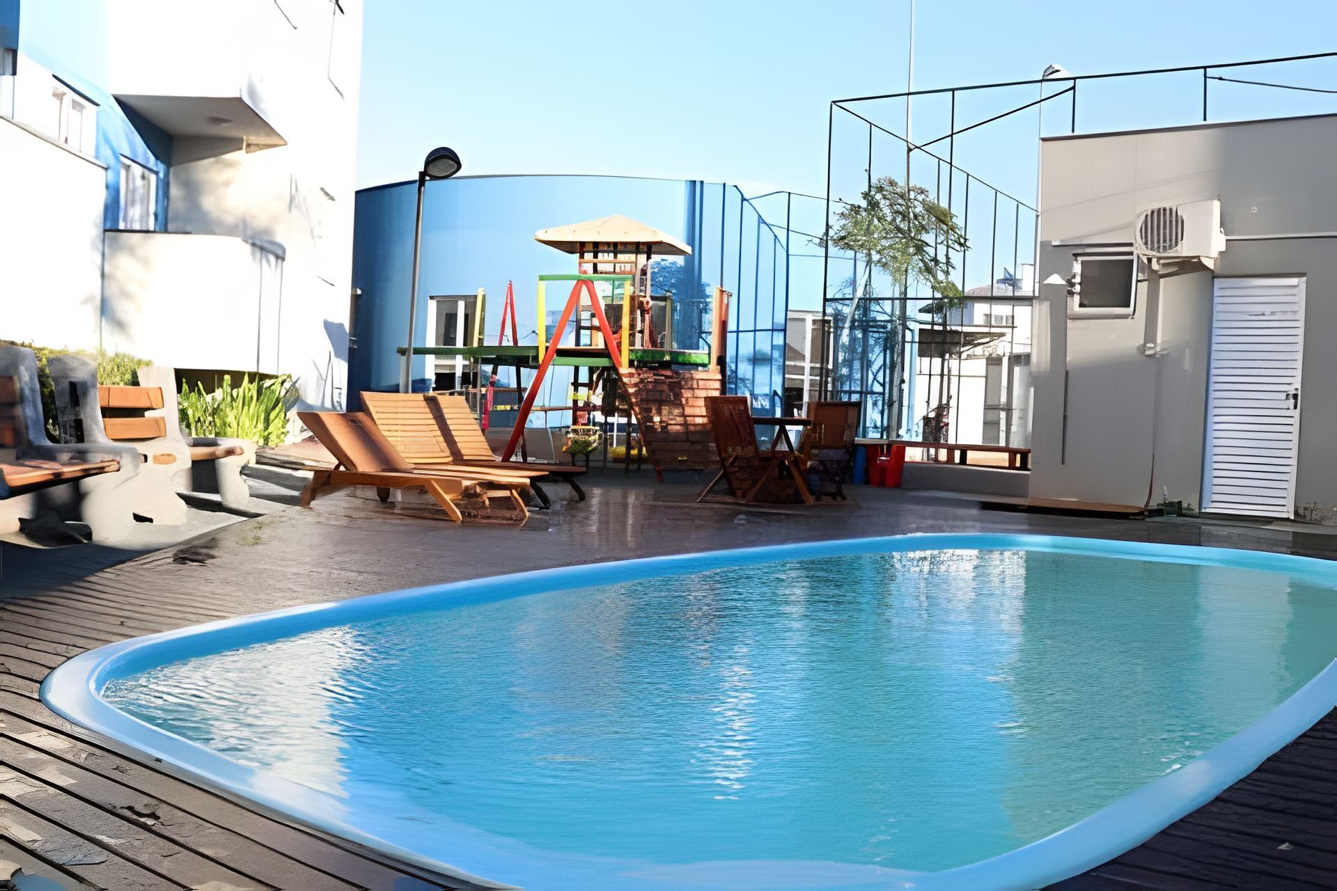 Una piscina con sillas de descanso, un parque infantil y un ventanal grande.