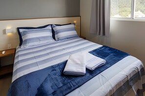 A neatly made bed with striped bedding, a folded towel, and a nightstand with a lamp. - Curta Praia do Quilombo - Lunata (Penha)