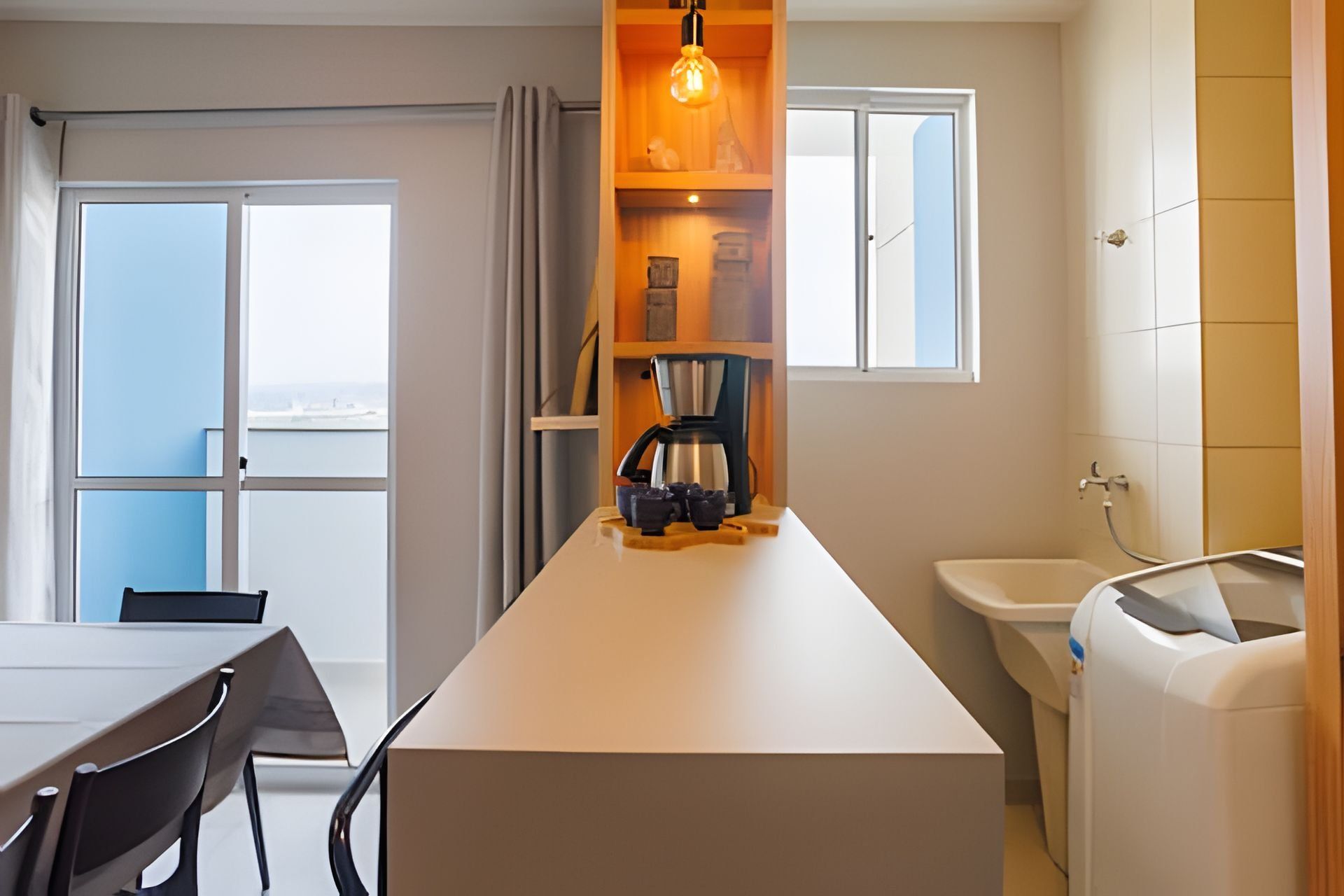 A modern kitchen with a coffee machine, a dining area with a table and chairs, and a view through a window.