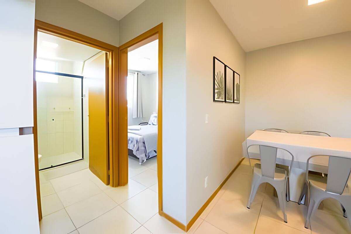 A hotel room with a bed, a bathroom, a dining area with a table and chairs, and a hallway leading to another room.