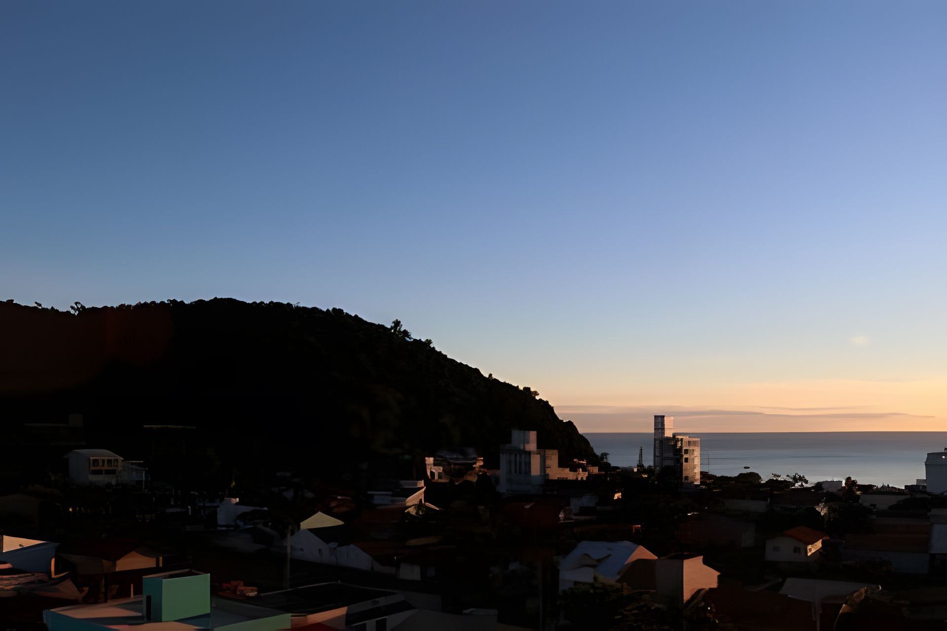 A coastal town with buildings, a hill, and the sea.