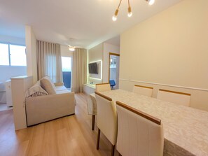 A modern hotel room with a sofa, dining table, chairs, a TV mounted on the wall, and a balcony with curtains. - Curta Praia do Quilombo - Lunata (Penha)