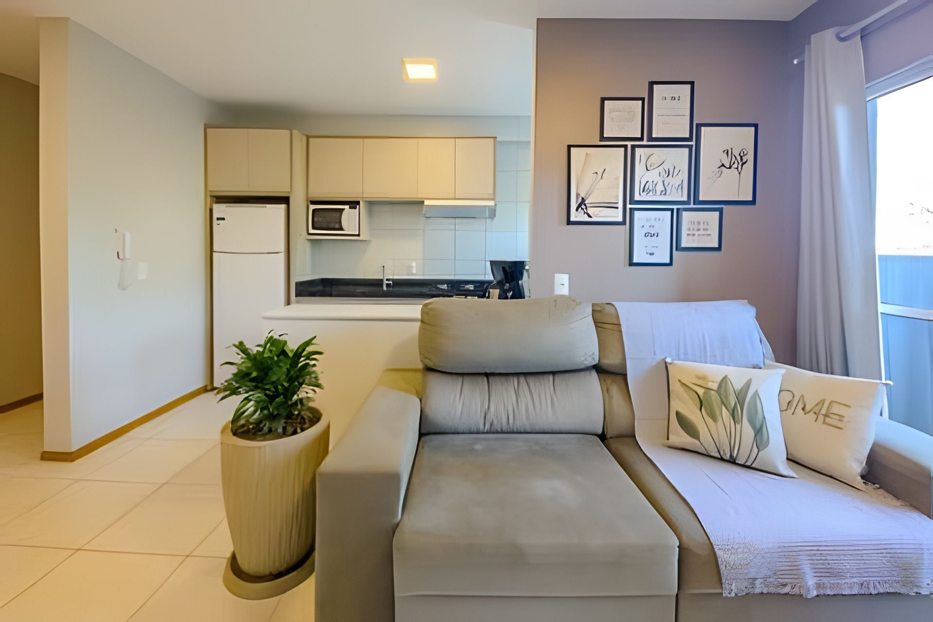 A modern living room with a sofa, a potted plant, and a kitchen in the background.