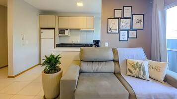 A modern living room with a sofa, a potted plant, and a kitchen in the background.
