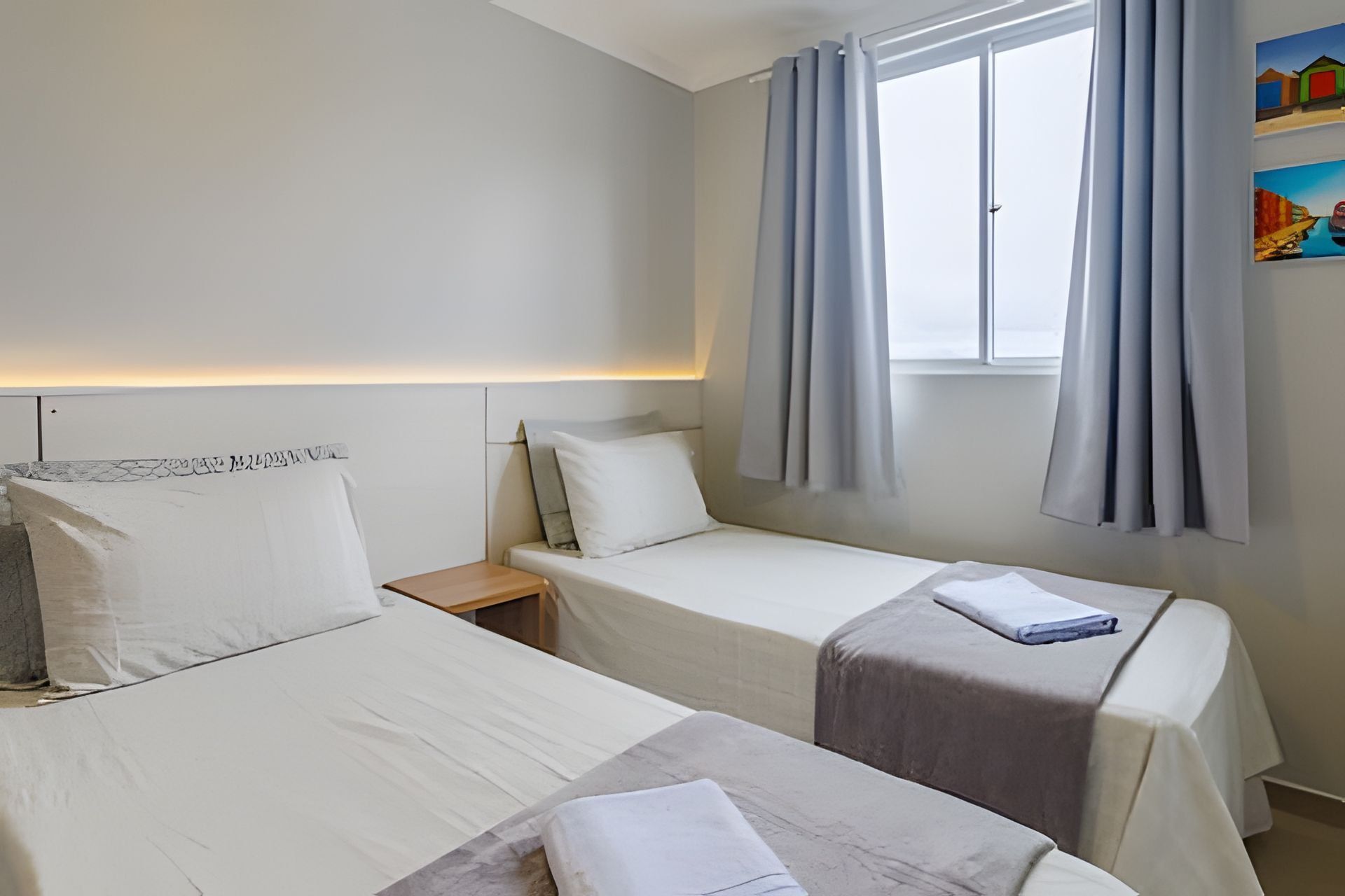 Una habitación de hotel con dos camas individuales, una mesita de noche, una ventana con cortinas y un cuadro en la pared.