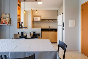 A modern kitchen with a dining area, including a table with chairs, a microwave, and a refrigerator. - Curta Praia do Quilombo - Lunata (Penha)