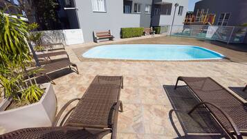 A pool area with lounge chairs, a small pool, and a building in the background.