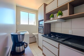 A compact kitchen with a coffee maker, a microwave, and a stove. There are cabinets and a window. - Curta Praia do Quilombo - Lunata (Penha)