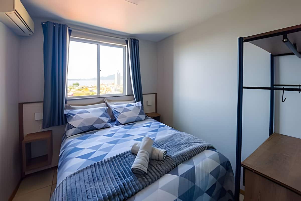 A bedroom with a bed, a window with curtains, a bedside table, and a hanging light fixture.