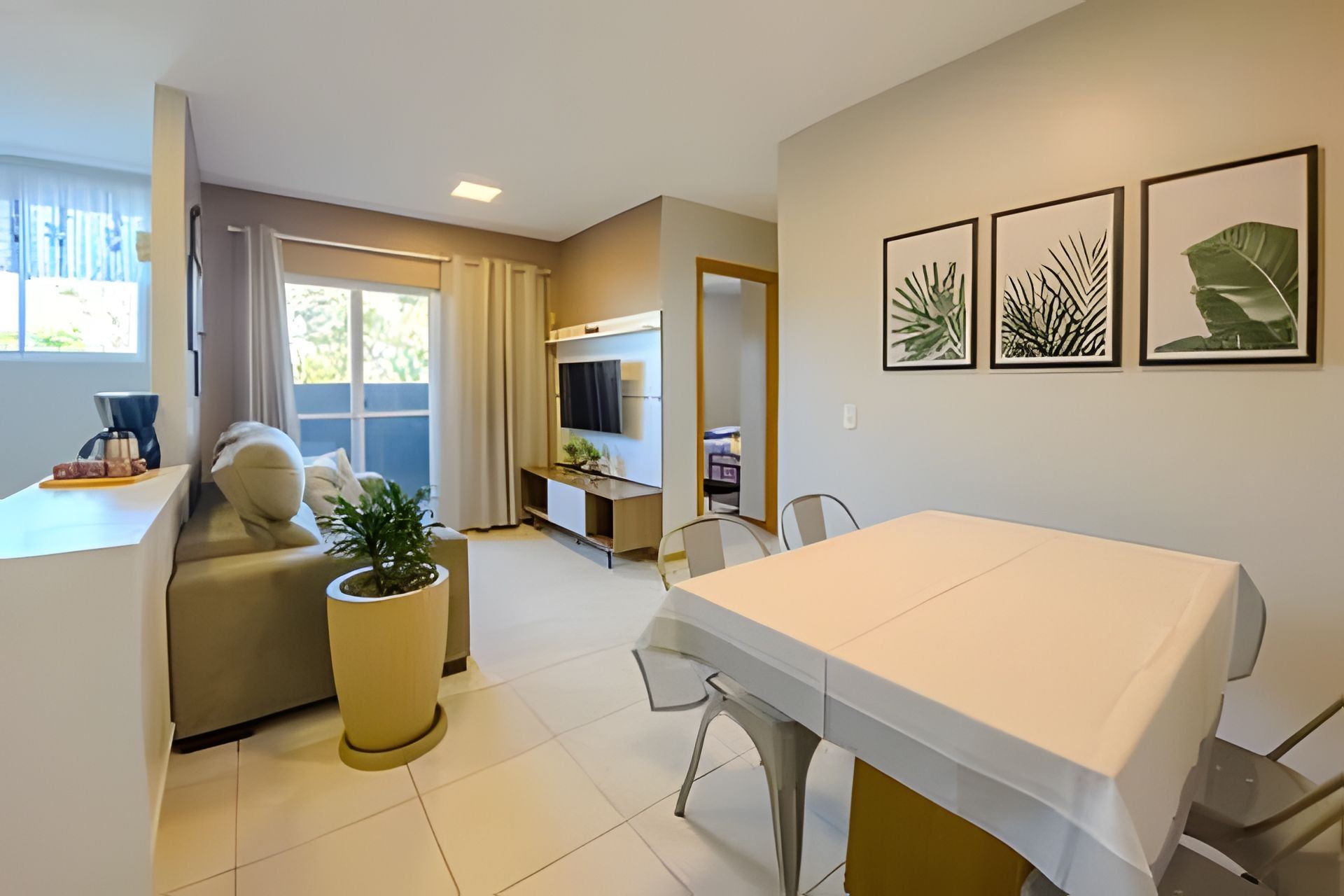A modern room with a dining table, a sofa, a potted plant, and artwork on the wall.