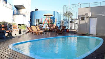 Una piscina con cubierta de madera, sillas de descanso y un parque infantil.