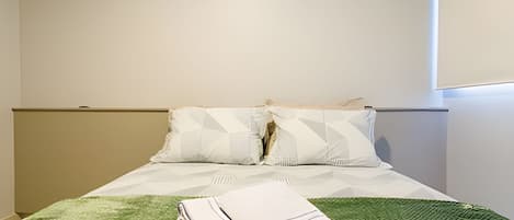 Ein Bett mit grüner Decke, zwei Kissen und einem gefalteten Handtuch.