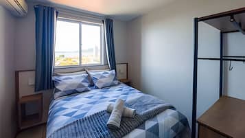 Un dormitorio con cama, ventana con cortinas, mesita de noche y lámpara colgante.