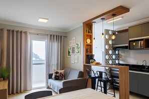A modern kitchen with a dining area, a sofa, and a view of the city. - Curta Praia do Quilombo - Lunata (Penha)