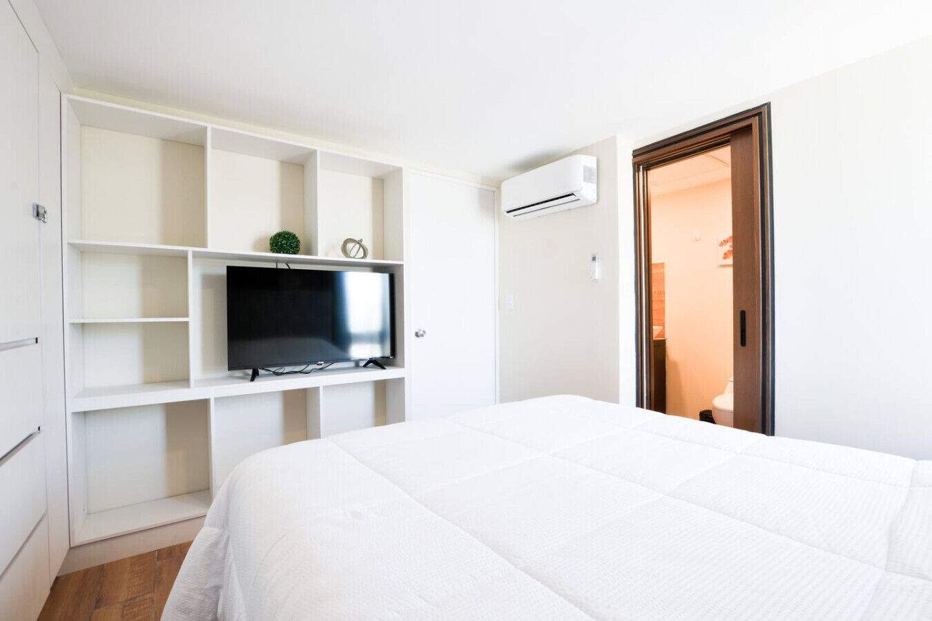 Ein Hotelzimmer mit einem Bett, einem an der weißen Wand befestigten Fernseher, einem Kleiderschrank und einer Klimaanlage.