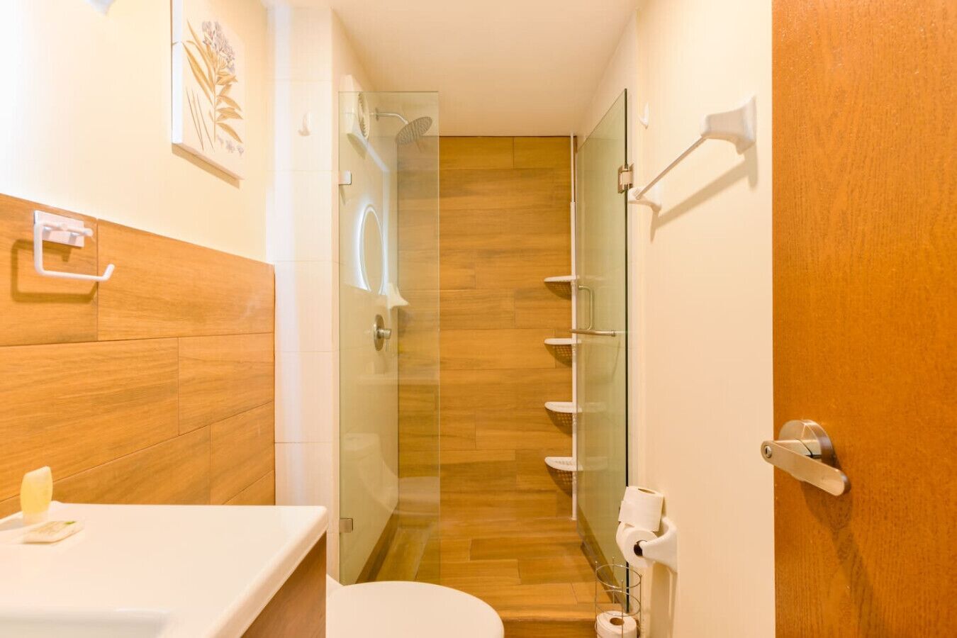 Une salle de bain moderne avec un plancher en bois, une douche en verre et des toilettes blanches.