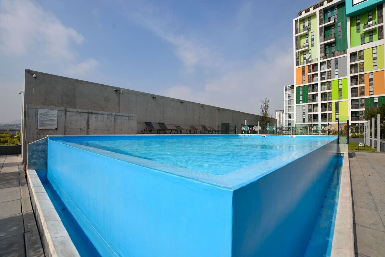 A rooftop swimming pool with a concrete wall and lounge chairs.