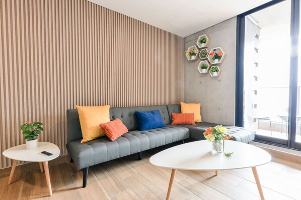 Ein modernes Wohnzimmer mit einem grauen Sofa, bunten Kissen, einem runden weißen Tisch und einem Blumentopf.