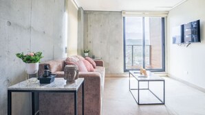 Uma sala de estar moderna com uma parede de concreto, um sofá rosa, uma mesa de centro de mármore e uma grande janela com vista para a cidade.