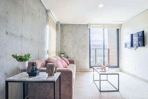 Ein modernes Wohnzimmer mit einer Betonwand, einem rosafarbenen Sofa, einem Marmortisch und einem großen Fenster mit Blick auf die Stadt.