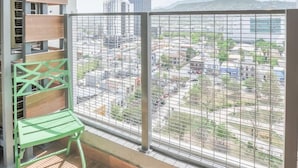Uma varanda com vista para a paisagem urbana, corrimão de metal e uma cadeira verde.