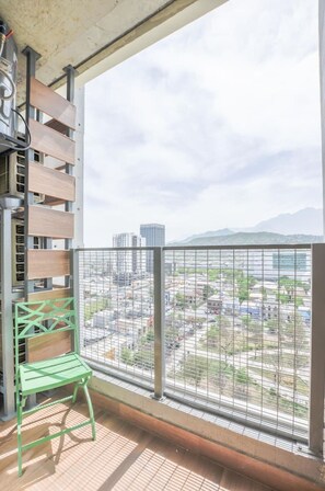 Ein Balkon mit Blick auf eine Stadtlandschaft, einem Metallgeländer und einem grünen Stuhl.