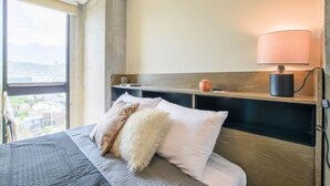 Une chambre d’hôtel avec un lit, une table de chevet, une lampe et une vue sur la ville.