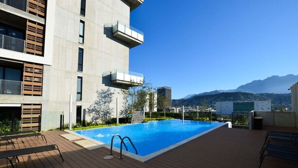 Une piscine sur le toit offrant une vue dégagée sur les montagnes, un bâtiment moderne doté de balcons et une terrasse en bois.