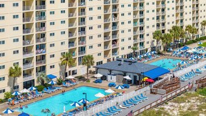 Un hotel de varios pisos con área de piscina en la azotea, que incluye sillas de sol, sombrillas y un puesto de salvavidas.