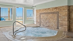 Zona de spa con bañera de hidromasaje, paredes con azulejos y vistas a la piscina exterior.