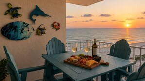 Una mesa con vistas al océano al atardecer, decorada con arte mural de temática marina, una tabla de quesos y copas de vino.