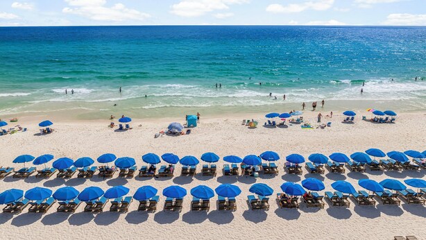 Una playa con filas de tumbonas y sombrillas, un mar azul cristalino y una orilla de arena.