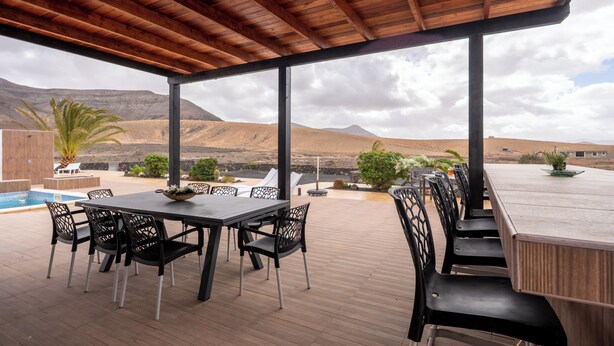 Een overdekt terras met een zwembad, stoelen en een tafel.