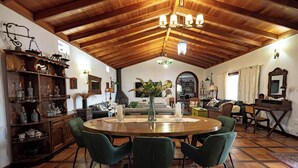 Een ruime woonkamer met een hoog houten plafond, een ronde houten eettafel met vier stoelen, en een gezellige zithoek met een bank en fauteuils.