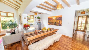 A spacious living area with a wooden bench, a sofa, and a dining table with a basket of fruit and a pitcher of juice.