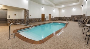 An indoor swimming pool with a stone wall, a no diving sign, and a seating area with chairs.