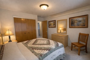 A bedroom with a bed, dresser, chair, and two framed pictures on the wall.