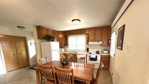 A kitchen with wooden cabinets, a dining table with chairs, a refrigerator, an oven, and a window with blinds. - Rocky Cliff 3 bedroom/2 bath home located in the town of Hill City! (Hill City)
