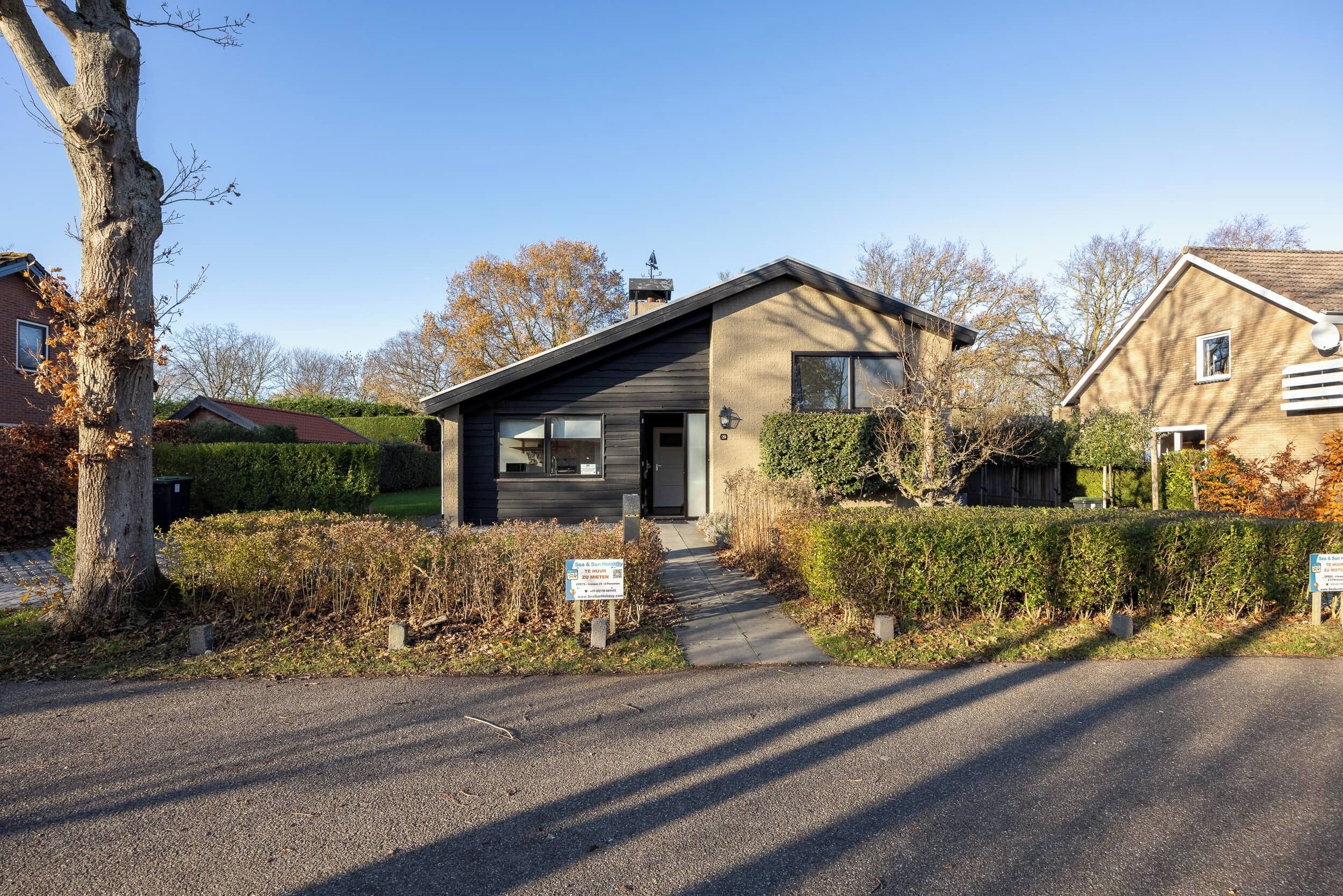 Een modern huis met twee verdiepingen, een donkere gevel, een duidelijke voordeur en een pad naar de ingang.