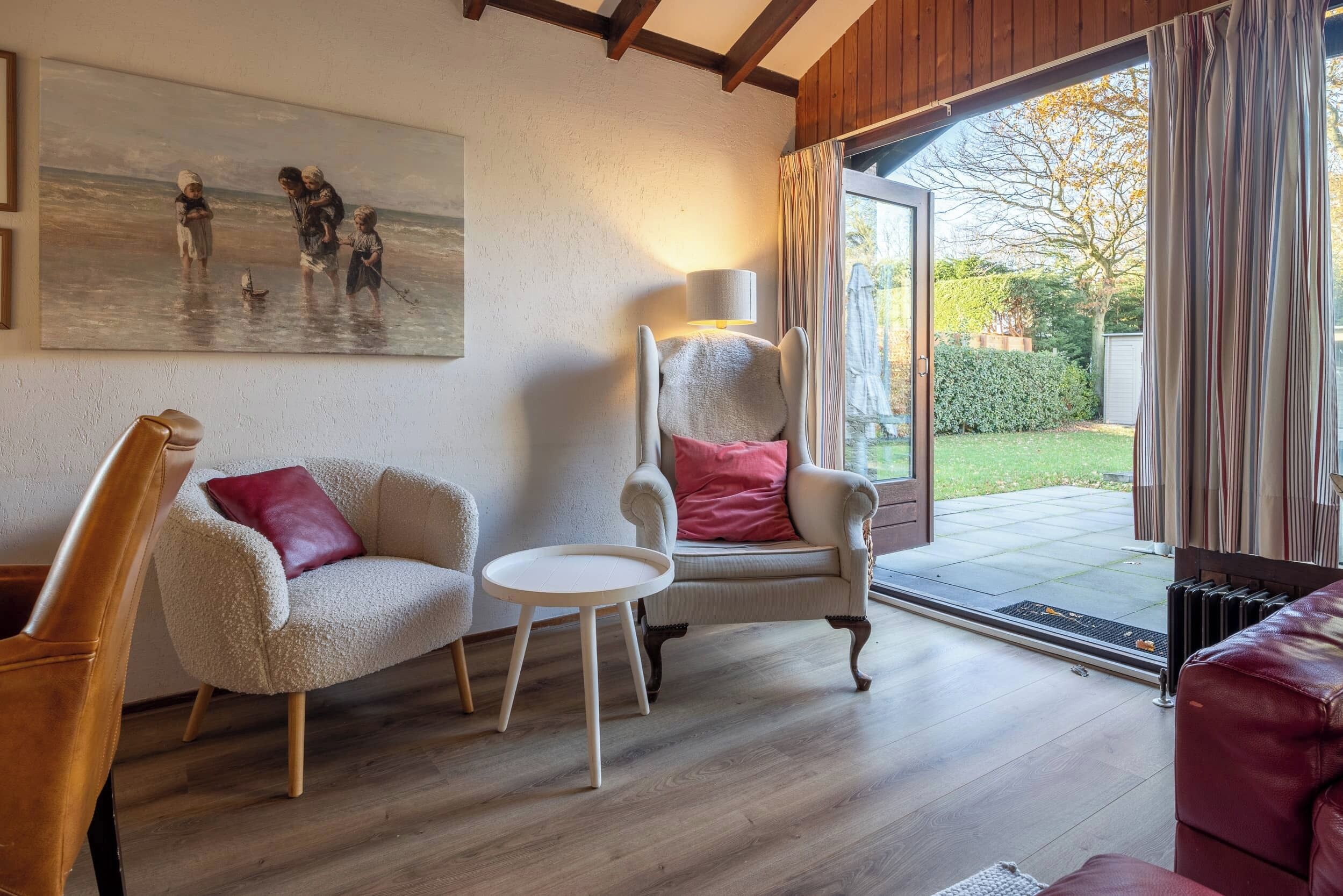 A cozy living room with a painting, a lamp, and a view of the outdoors.
