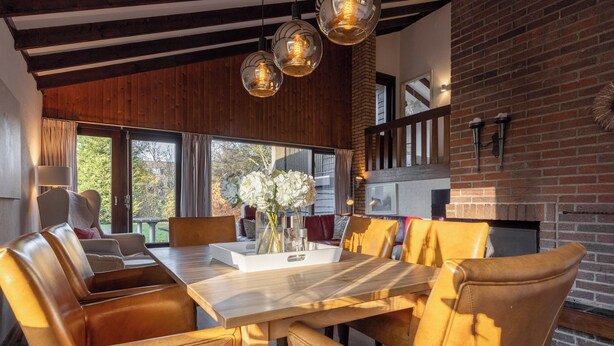 Un'area pranzo moderna con sedie in pelle, un tavolo in legno e luci a sospensione.