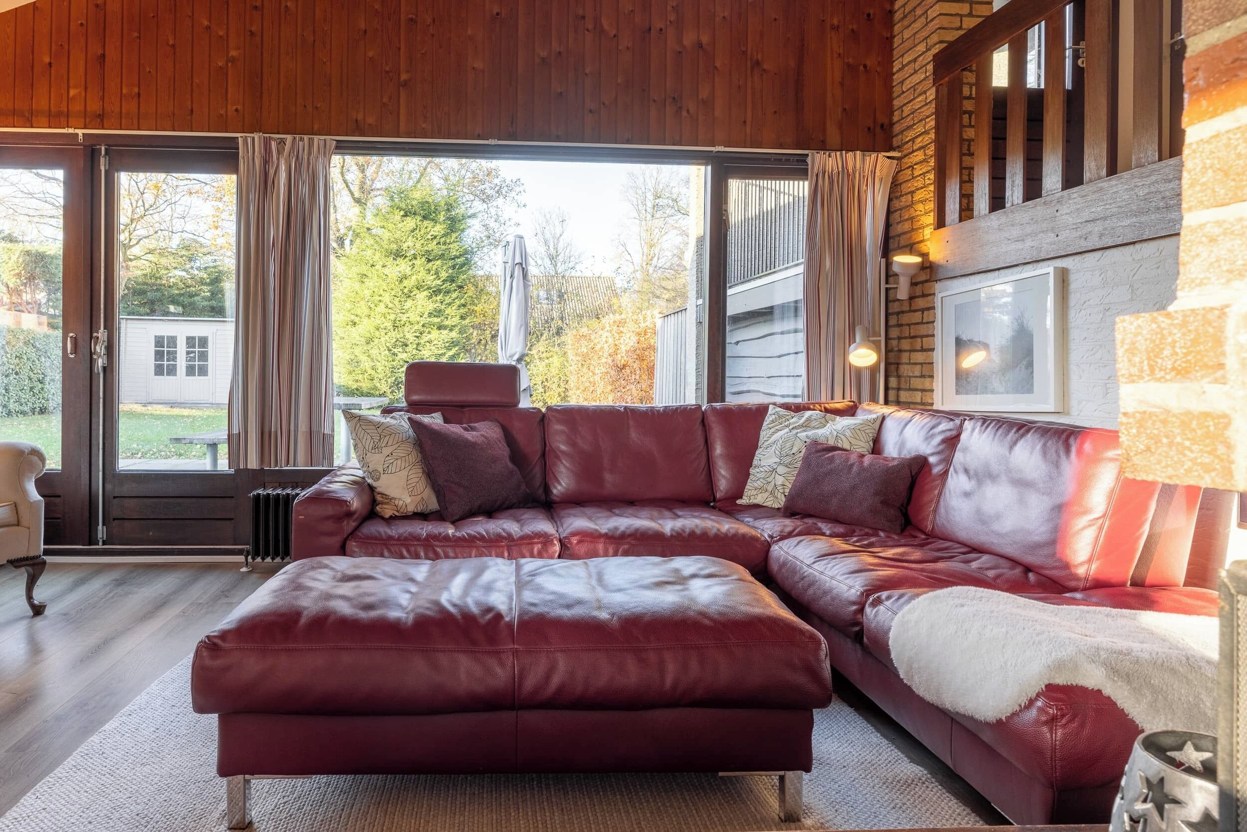 A red leather sectional sofa with a white throw blanket, a radiator, and a view of the outdoors through large windows.