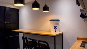 A small kitchenette with a wooden countertop, three pendant lights, a white container with a blue lid, and two black chairs.