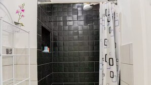 A bathroom with black tiled walls, a shower curtain, and a white shelf with a decorative item.
