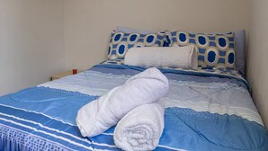 A bed with blue and white bedding, two white towels, and patterned pillows.