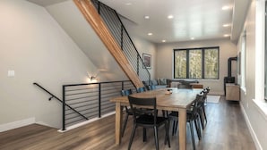 A modern interior with a dining area, a staircase, and a view of trees through large windows. - Private Hot Tub | Steps to Trails & Town | Foosball (Winter Park)