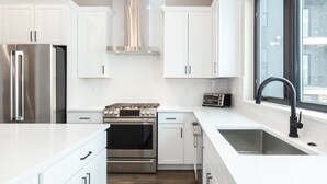 A modern kitchen with white cabinetry, stainless steel appliances, a built-in oven, a toaster, and a large window providing natural light. - Private Hot Tub | Steps to Trails & Town | Foosball (Winter Park)