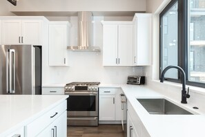 A modern kitchen with white cabinetry, stainless steel appliances, a built-in oven, a toaster, and a large window providing natural light. - Private Hot Tub | Steps to Trails & Town | Foosball (Winter Park)