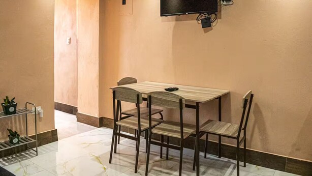 Habitación de hotel con una mesa y sillas de madera, un televisor de pantalla plana en la pared y una puerta que da a otra habitación.